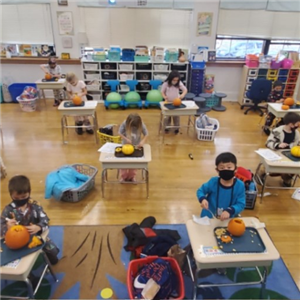 Six kindergartners at their desks in the classroom carving pumpkins 